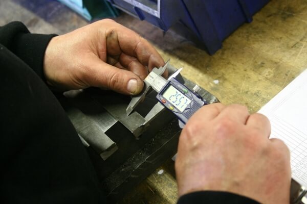 Hands using a digital caliper to inspect a machined metal component